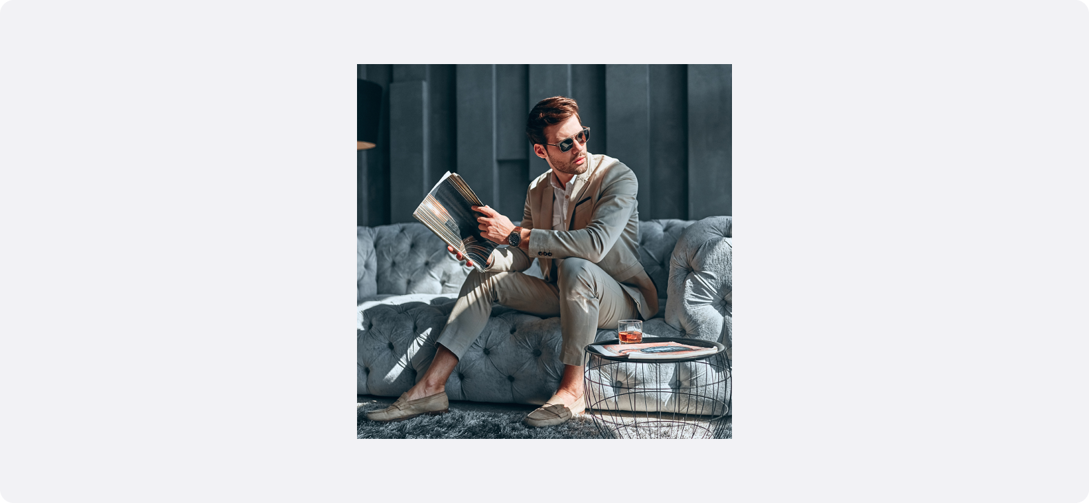 ソファに座り雑誌を読むスーツ姿の男性を写した、上質なライフスタイルを想起させるビジュアル
