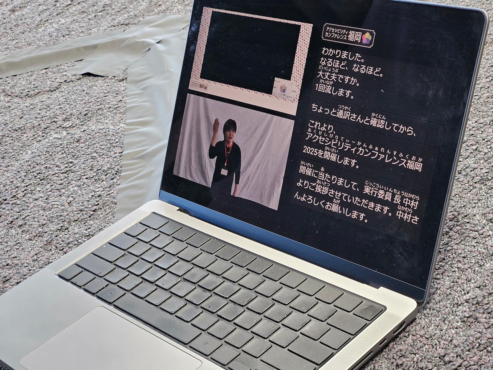 手話通訳やライブ字幕が表示されているノートパソコンの写真。現在表示しているスライド、手話通訳者、音声書き起こしテキストが画面を分割して表示されている。