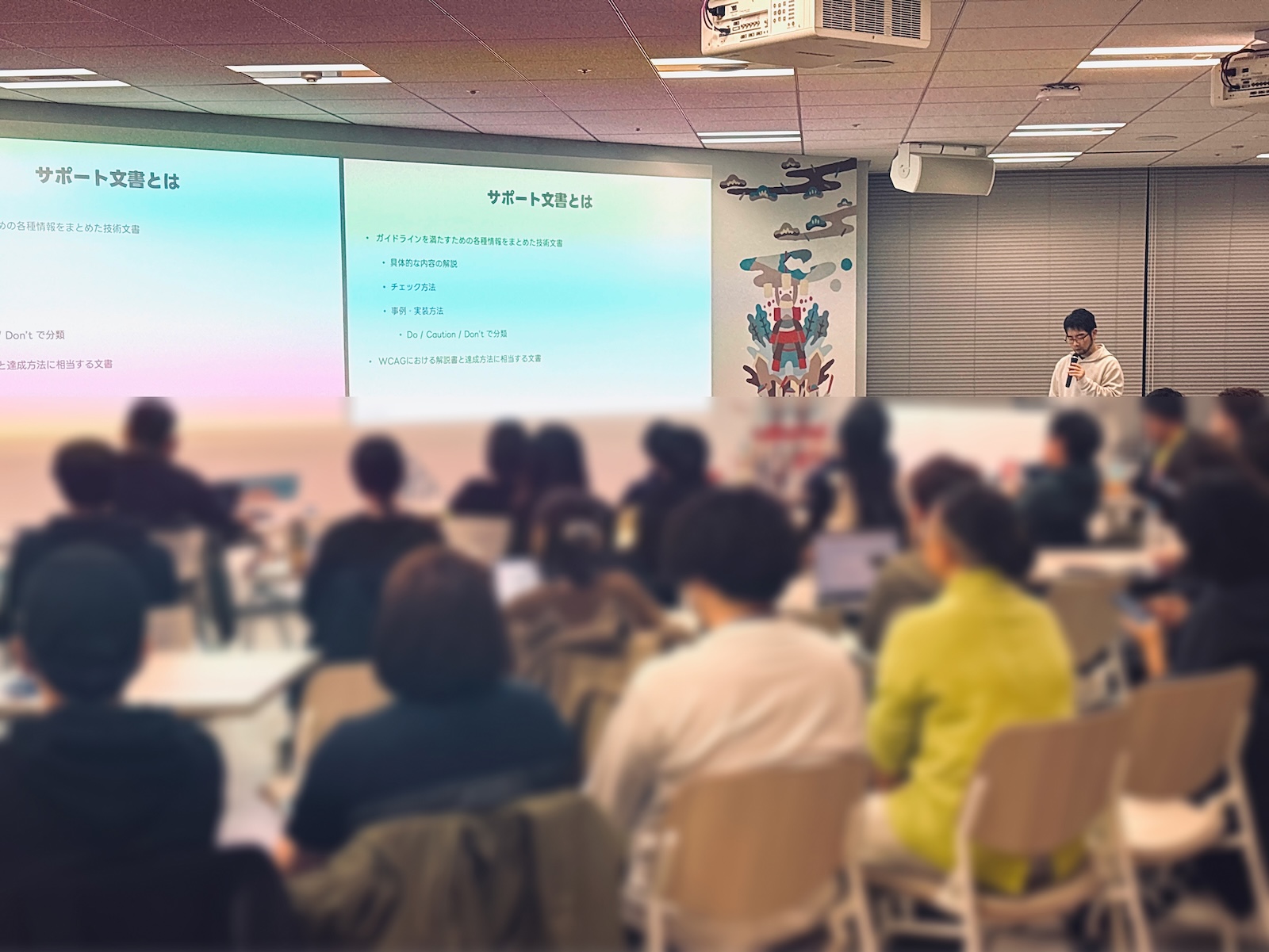 前夜祭の会場写真。写真奥にはLINEヤフー中野が登壇しており、スライドが壁面に大写しになっている。手前の客席は参加者でほぼ埋まっている。